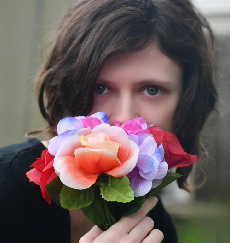A picture of Wynn.E partially covering their face with a bouquet of flowers.